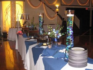 a glass centerpiece with blue and green marbles set up near a catering buffet station