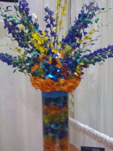 a blue and yellow floral arrangement in a matching vase with orange trim used at a catering event