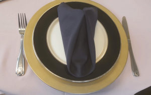 catering black trimmed plate on top of a gold plate with white napkin