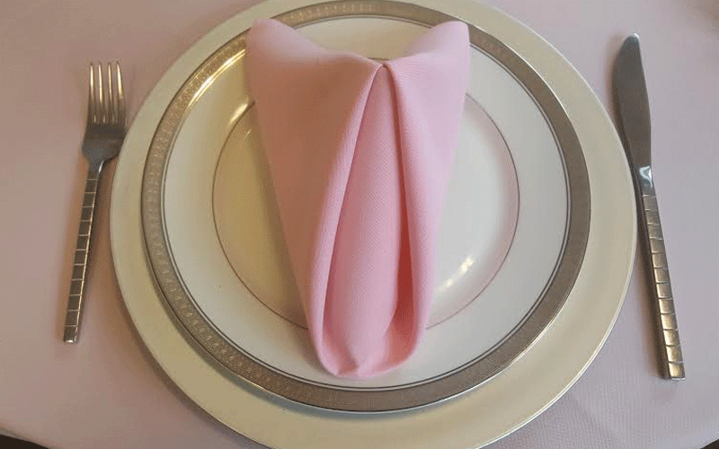 cream colored plates with gold trim and a pink napkin for catering
