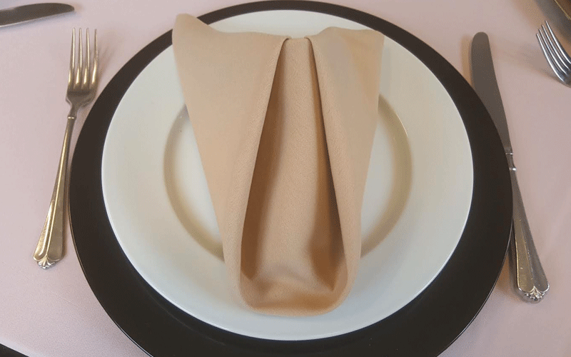 a white plate on top of a black plate with peach napkin for catering